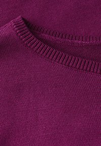 Lila gestrickter Pullover mit einem gerippten Ausschnitt und glatter Textur. Nahaufnahme, die subtile Stickdetails und ein gleichmäßiges Stoffmuster zeigt.