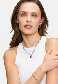 Färgglad pärlprydnad som inkluderar ett halsband med en silverberlock och ett matchande armband. Modellen bär matchande örhängen.