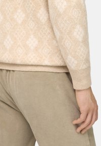 Pull en maille beige avec un motif en losanges, poignets et ourlet côtelés. Associé à un pantalon en velours côtelé beige clair, mettant en valeur une texture douce.