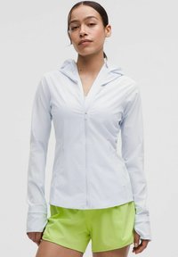 Light blue zip-up athletic jacket with a hood, made from smooth fabric. Features long sleeves with thumb holes, paired with bright green shorts.