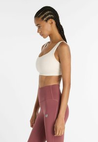 Sujetar deportivo beige con tirantes anchos, combinado con mallas de tiro alto color granate con un pequeño logo, textura suave y diseño ajustado.