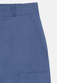 Modré bavlnené nohavice so štruktúrovanou tkaninou, elastickým pásom, dvoma vreckami a malým logom Nike swoosh blízko vrecka.
