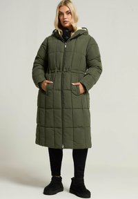 Olivgrön vadderad kappa med huva, med dragkedjestängning, sidofickor och cinchad midja. Mjuk innerfoder och quiltad design.