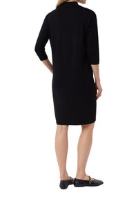 Schwarzes gestricktes Kleid mit rundem Ausschnitt, drei Viertelärmeln und geradem Schnitt. Getragen mit schwarzen flachen Schuhen.