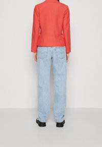 Röd kavaj med strukturerade axlar, i kombination med ljusblå baggy jeans. Jeansen har en subtil tvätt och detaljer på bakfickorna. Svarta klumpiga skor.