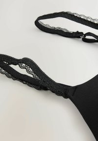 Sostén negro con tirantes de encaje texturizado, herrajes ajustables y un cuerpo de tela suave, que enfatiza un diseño minimalista.