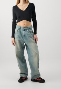 Black ribbed cropped long-sleeve top paired with light blue oversized denim jeans. Black sneakers with red accents completed the outfit.