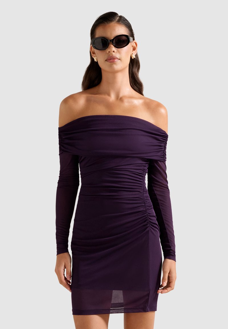 Μωβ φόρεμα με τους ώμους ακάλυπτους, μακριά μανίκια, ρυτιδιασμένη υφή, εφαρμοστή γραμμή και διάφανο τελείωμα στο κάτω μέρος. Μοντέλο φορά γυαλιά ηλίου.