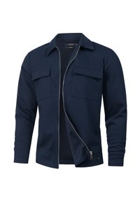 Marineblå zip-up jakke med lange ærmer, to brystlommer og en glat tekstur. Har krave og en subtil detalje med en frontløsning.