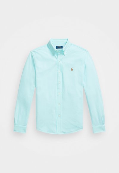 Camisa de botão azul claro feita de algodão, com colarinho clássico, mangas longas e logotipo bordado no lado esquerdo do peito.