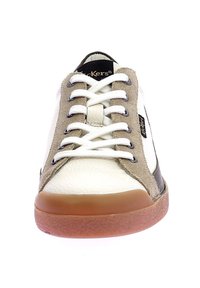 Zapatilla de cuero blanca con acentos de gamuza beige, detalles en negro y suela de goma. Presenta cordones blancos y un diseño de punta redondeada.
