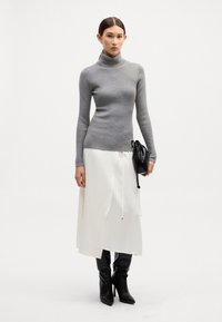 Grau gerippter Rollkragenpullover, weiße Midikleid, schwarze Stiefel mit Absatz und eine kleine schwarze Handtasche mit Kordelzugdetails. Einheitlicher weißer Hintergrund.