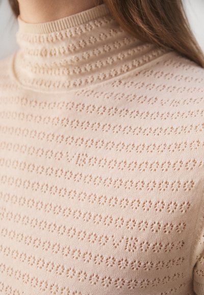 Adītas turtlenecks džemperis maigi rozā krāsā, ar teksturētu rakstu, kas sastāv no mazām ziedu formām un vertikālām svītrām.