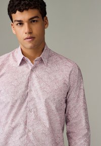 Camicia rosa chiaro con bottoni e motivo bianco dettagliato. Colletto standard, maniche lunghe e chiusura frontale con bottoni.