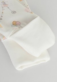 Pigiama in cotone con un leggero motivo pastello che presenta palloncini e personaggi, abbinato a polsini bianchi a coste. Tessuto morbido e vestibilità comoda.