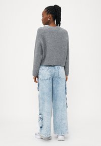 Maglione grigio lavorato a maglia con un design cropped, abbinato a jeans cargo blu chiaro con grandi tasche e vestibilità rilassata.