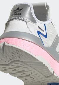 Białe buty sportowe z metalicznym srebrnym obcasem, niebieskimi akcentami i różową podeszwą środkową. Posiadają teksturowaną powierzchnię i logo z tyłu. Masywna biała podeszwa.