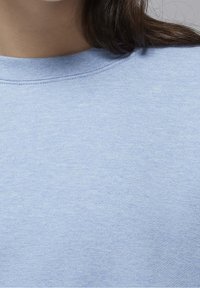 Sudadera azul clara hecha de una tela suave, con un clásico escote redondo y puños acanalados. Textura suave con un sutil patrón jaspeado.