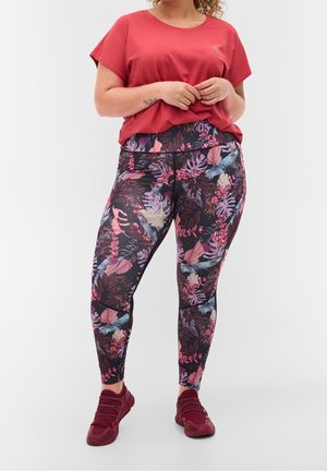 Czerwony top z krótkim rękawem w połączeniu z legginsami w kwiatowy wzór na ciemnym tle, z różowymi i niebieskimi liśćmi, oraz bordowymi butami sportowymi.