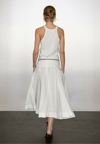 Débardeur blanc sans manches associé à une jupe fluide arrivant aux chevilles. La jupe présente des plis et une bordure contrastante à l'ourlet.