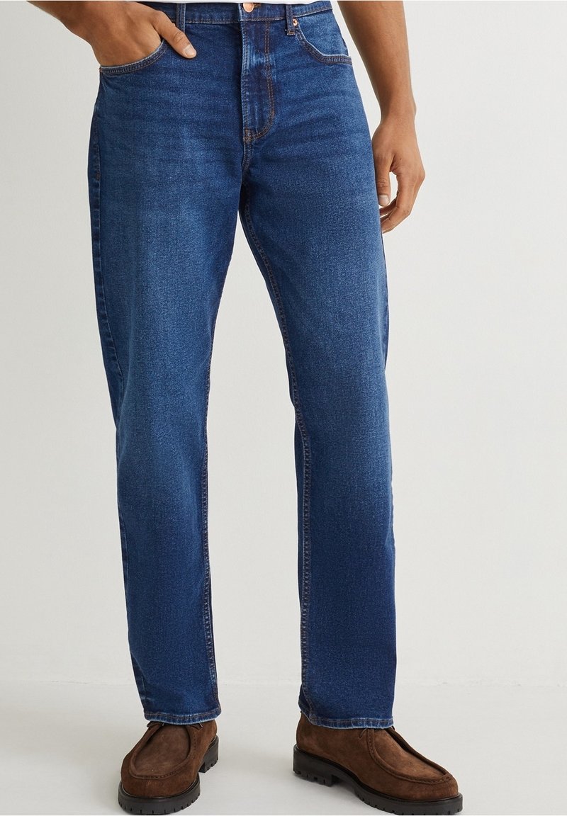 Blå denimjeans med rak passform, med dragkedja, två framfickor och en klassisk femficksdesign. Bruna mockaskor.