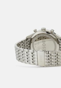 Montre en acier inoxydable argenté avec un bracelet à maillons, un boîtier rond, des fonctionnalités de chronographe et une finition polie. Étanche jusqu'à 5 bars.