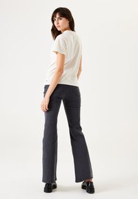 Camiseta de algodón blanca combinada con unos jeans acampanados oscuros. Los jeans presentan un diseño clásico de cinco bolsillos y detalles de costura sutiles.