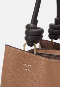 Sac fourre-tout en cuir couleur camel avec surface texturée, doté d'une anse boucle bicolore et de ferrures métalliques dorées. Des surpiqûres blanches soulignent les bords.