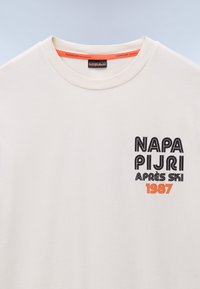 Hvid bomulds T-shirt med ribbet rund hals, prydet med sort og orange grafisk tekst "NAPAPIJRI APRES SKI 1987" på forsiden.