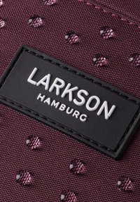 Tejido burdeos con un patrón texturizado, que presenta gotas en relieve y una etiqueta rectangular negra con "LARKSON HAMBURG" en letras blancas.