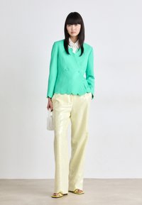 Een mintgroene scalloped blazer, een crèmekleurige satijnen blouse, glinsterende gele broek en felgele sandalen. Een handtas van witte parels.