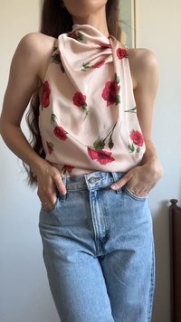 Floral blouse in light pink fabric with red roses, featuring draped neckline and fitted design, paired with high-waisted light blue jeans.