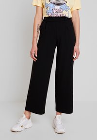 Černé kalhoty s širokými nohavicemi a vysokým pasem, vyrobené z měkké tkaniny. Obsahují boční kapsy, hladkou texturu a čistou siluetu.