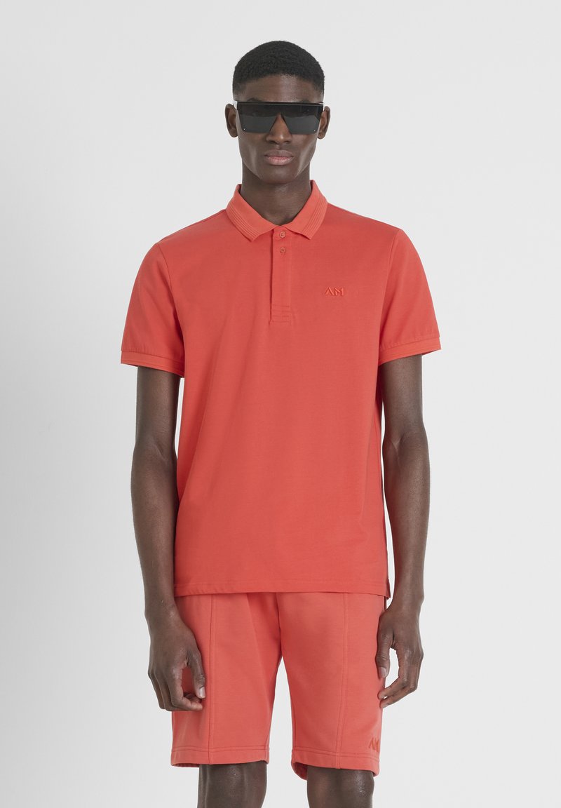 Rode polo met kraag en korte mouwen, gecombineerd met bijpassende shorts. Inclusief subtiele branding op de borst en een gladde textuur.
