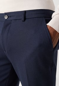 Marineblauwe broek van textuurstof, met een standaard tailleband, knoopsluiting en schuine zijzakken.