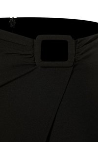Gros plan d'une jupe noire avec une boucle rectangulaire recouverte de tissu et des détails froncés près de la taille et de la fermeture éclair latérale.