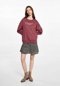 Felpa bordeaux con scritte bianche, abbinata a una gonna nera a fantasia. Stivaletti alla caviglia marroni completano l'outfit. Design flat e casual.
