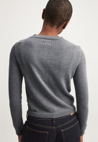 Gray knit sweater with a round neckline and ribbed cuffs. Close-fitting design with a soft texture, styled with dark jeans.