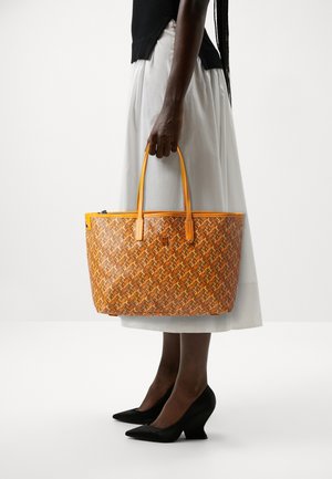 Borsa a tracolla arancione intrecciata con accenti gialli, di forma rettangolare e dotata di due manici robusti, esposta accanto a una gonna bianca.