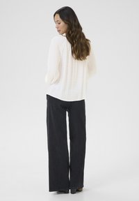 White, textured, long-sleeve blouse paired with dark wide-leg jeans, viewed from the back. Blouse features a loose fit and ribbed details.