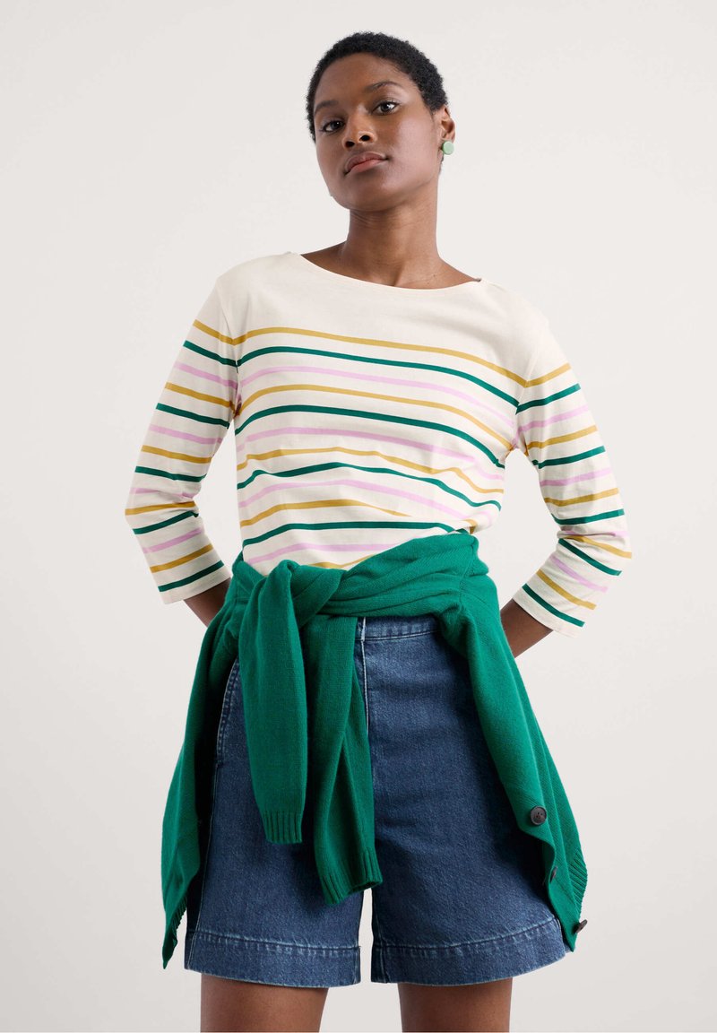 Striped long-sleeve top in cream, yellow, green, pink, and purple; paired with dark denim shorts; green sweater tied at the waist.