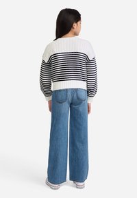 Balta ir tamsiai mėlyna dryžuota didelė megztinis su guma apačioje, derinamas su šviesiai mėlynomis plačios kojų džinsais ir baltais sportbačiais su raudonomis detalėmis.