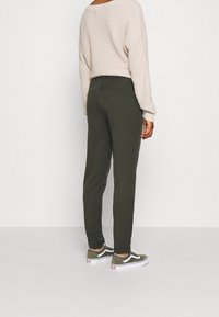 Olivgröna joggare med elastisk midja, som bärs med en beige texturerad tröja och gröna sneakers med vita detaljer.