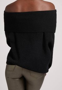 Maglione nero a spalle scoperte in maglia con scollatura a coste, vestibilità ampia e tessuto testurizzato, abbinato a pantaloni metallici verdi aderenti.