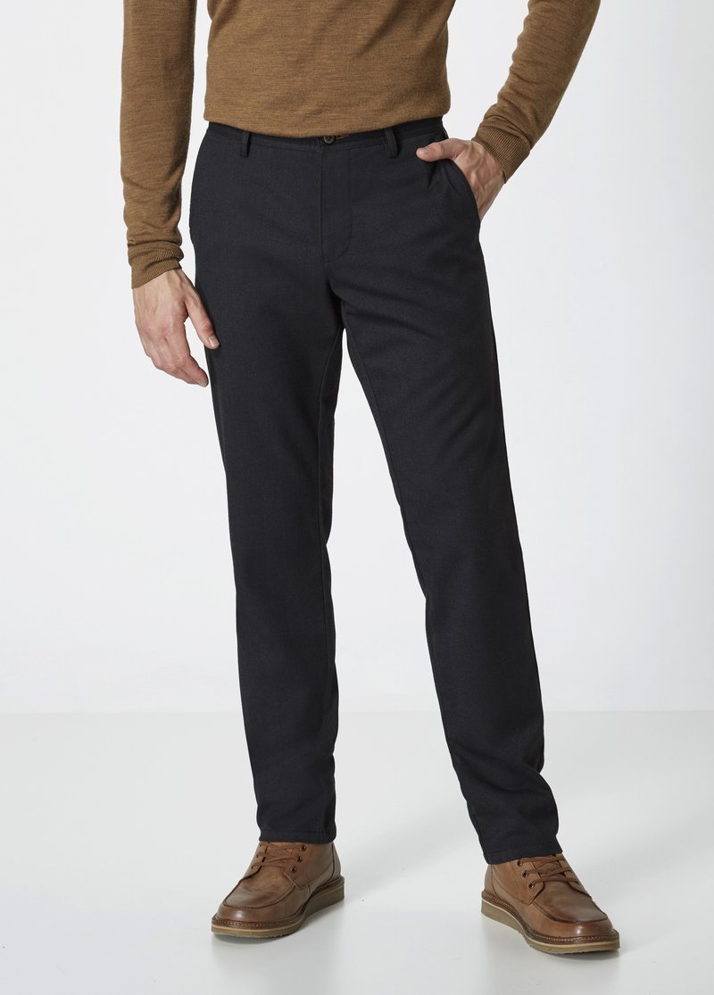 Dunkelblaue Hose, schmal geschnittenes Design, leichter Stoff mit leichter Textur, kombiniert mit braunen Lederschuhen. Schlichte Fronttaschen, Knopfverschluss.