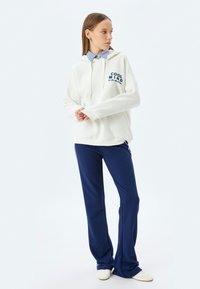Felpa bianca con scritta "COOL MIND", abbinata a pantaloni della tuta blu navy. Presenta una vestibilità comoda, coulisse e una camicia a righe sotto.