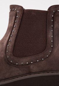 Botte Chelsea en daim marron avec panneau latéral élastique et détails à clous métalliques le long du bord.