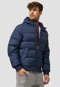 Chaqueta de plumón azul marino con capucha, que presenta un cierre frontal, diseño de paneles cosidos, puños elásticos y un logo en el cierre.