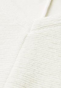 Tessuto bianco con texture e un aspetto stropicciato, caratterizzato da una cucitura visibile e un sottile motivo dimensionale.