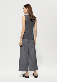 Gray knitted sleeveless top with a textured pattern, paired with loose, wide gray trousers, and black sandals. Simplistic, modern design.